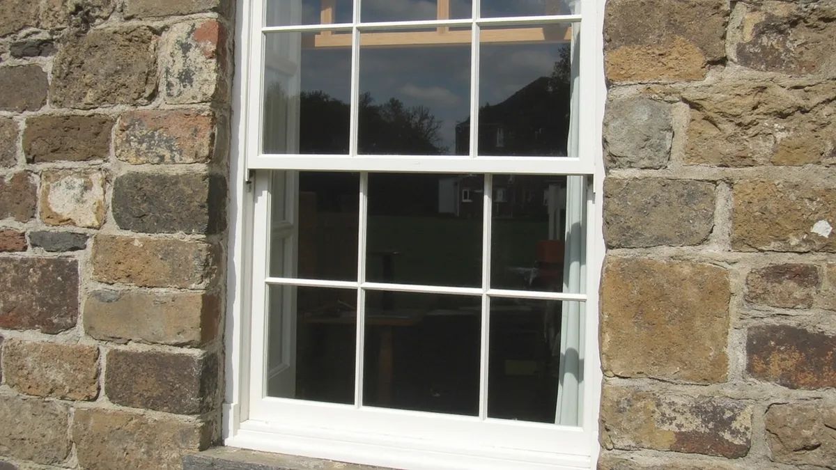Traditional Georgian six-over-six sash window with glazing bars in a stone facade.