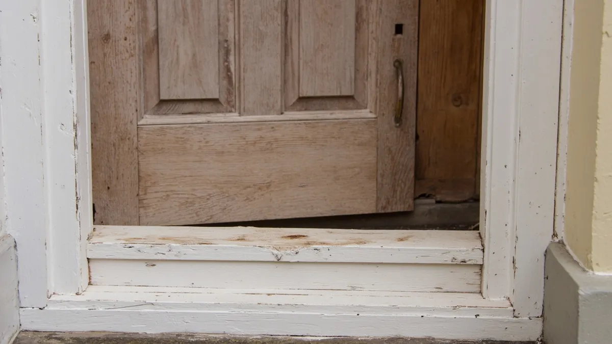 Weathered timber door above a worn painted threshold, where splash-back keeps the bottom rail wet